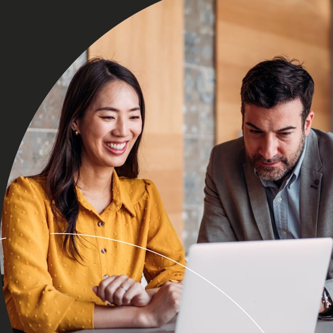 Diverse business professionals, an Asian woman and a man, smiling and collaborating intently on a laptop