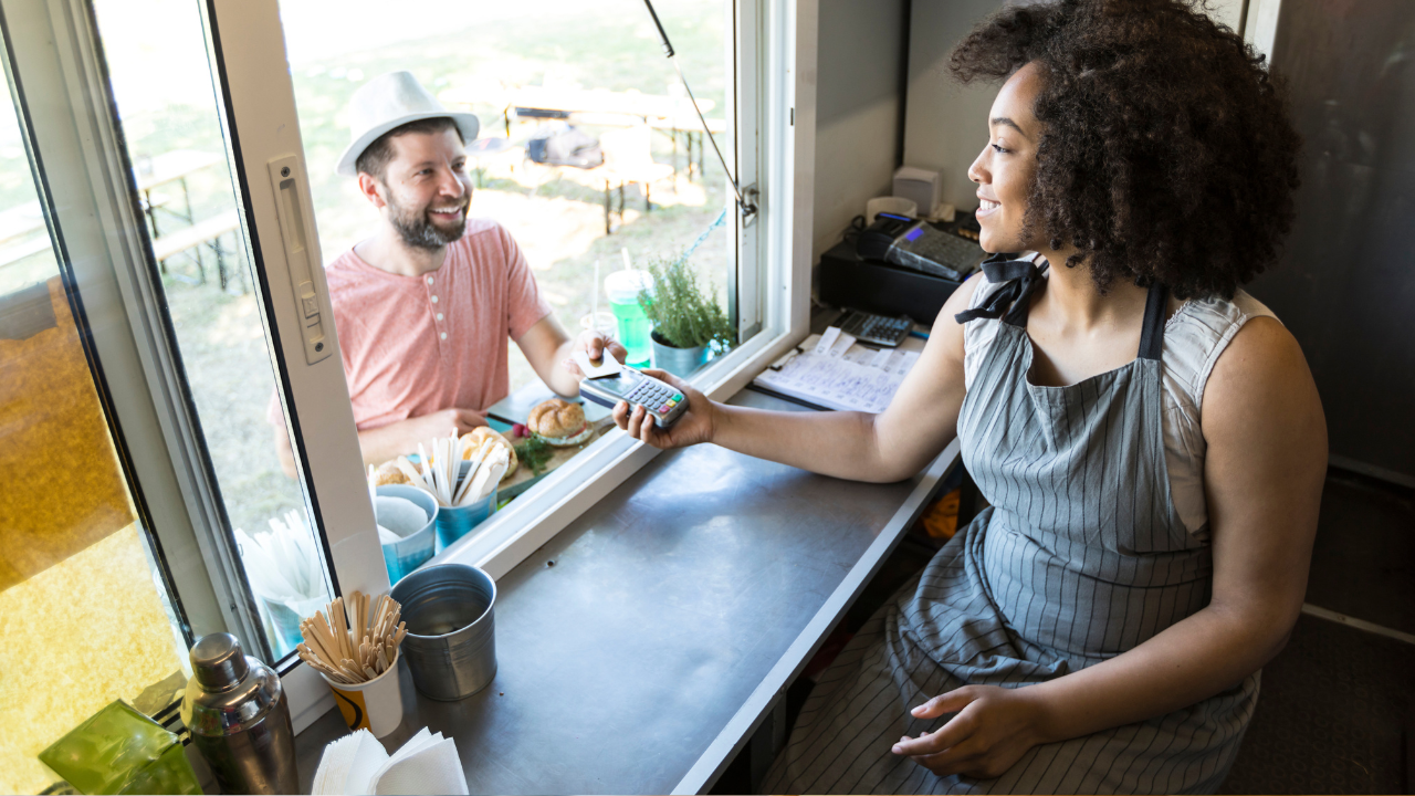 A woman in a food truck accepts a credit card from a customer. 