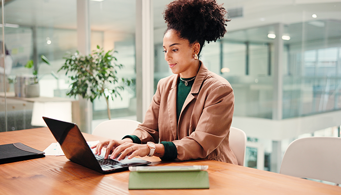 A woman in an office setting, focused on her laptop while seated at a desk