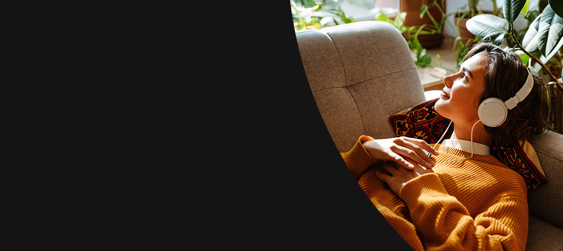 Woman on couch with headphones on looking out the window