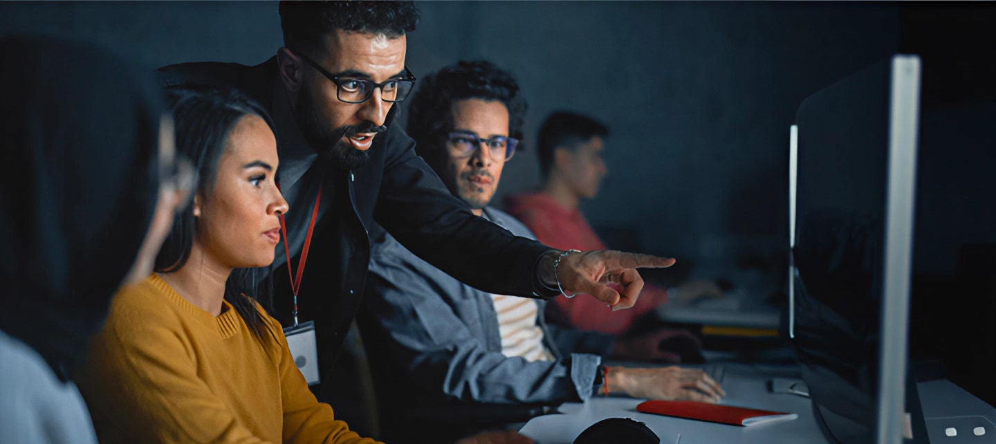 מורה מדריך שלושה סטודנטים ממוקדים בכיתה מוארת בעמימות.