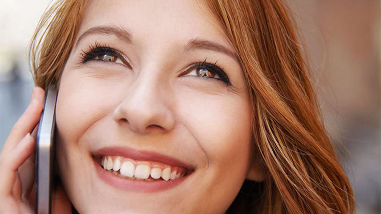 Et nærbillede af en kvinde, der smiler, mens hun taler i mobiltelefon.