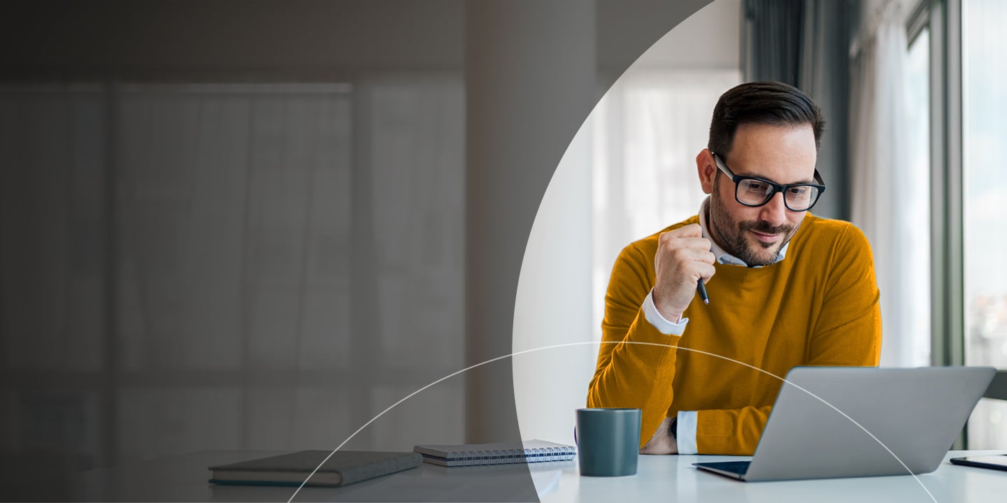 Mand med en kuglepen i hånden, som kigger på en laptop.
