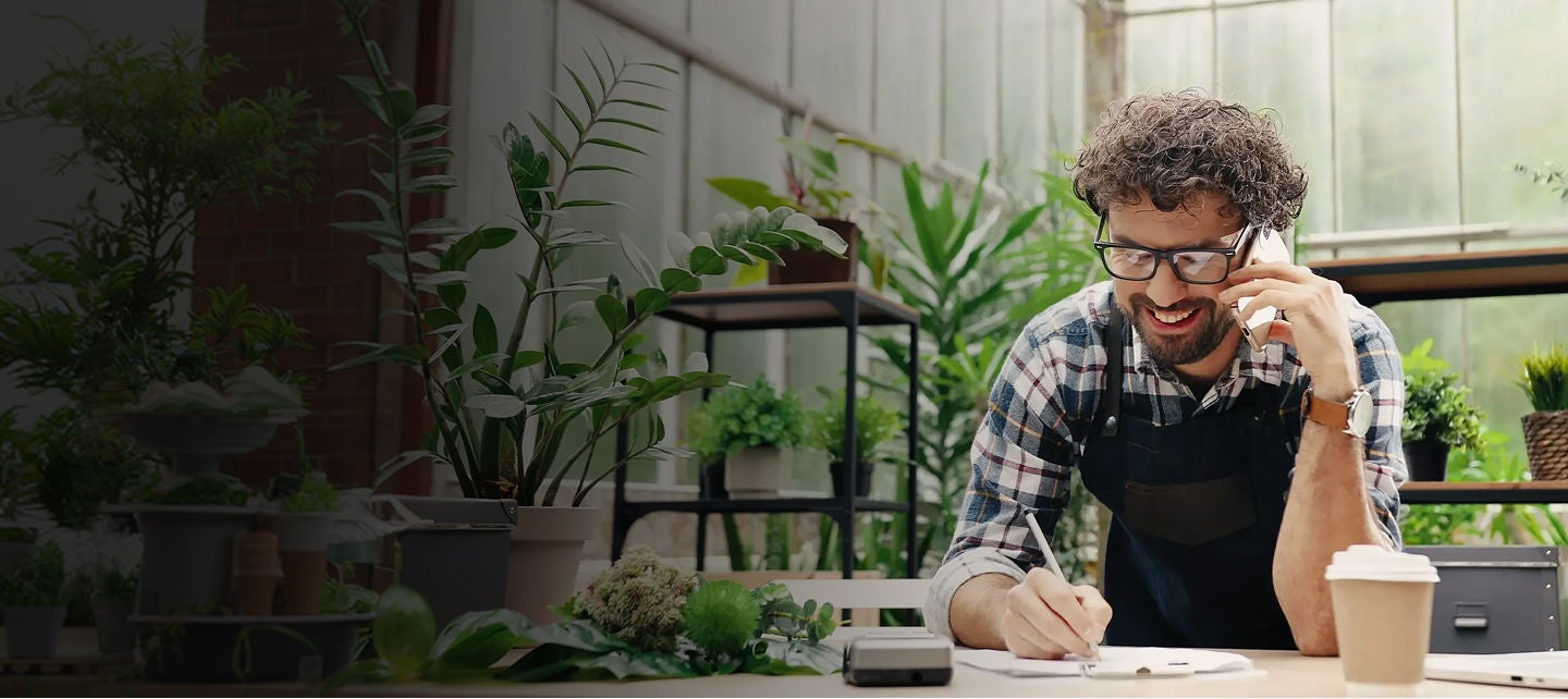 A man in a plaid shirt and glasses is writing on a piece of paper whilst on call