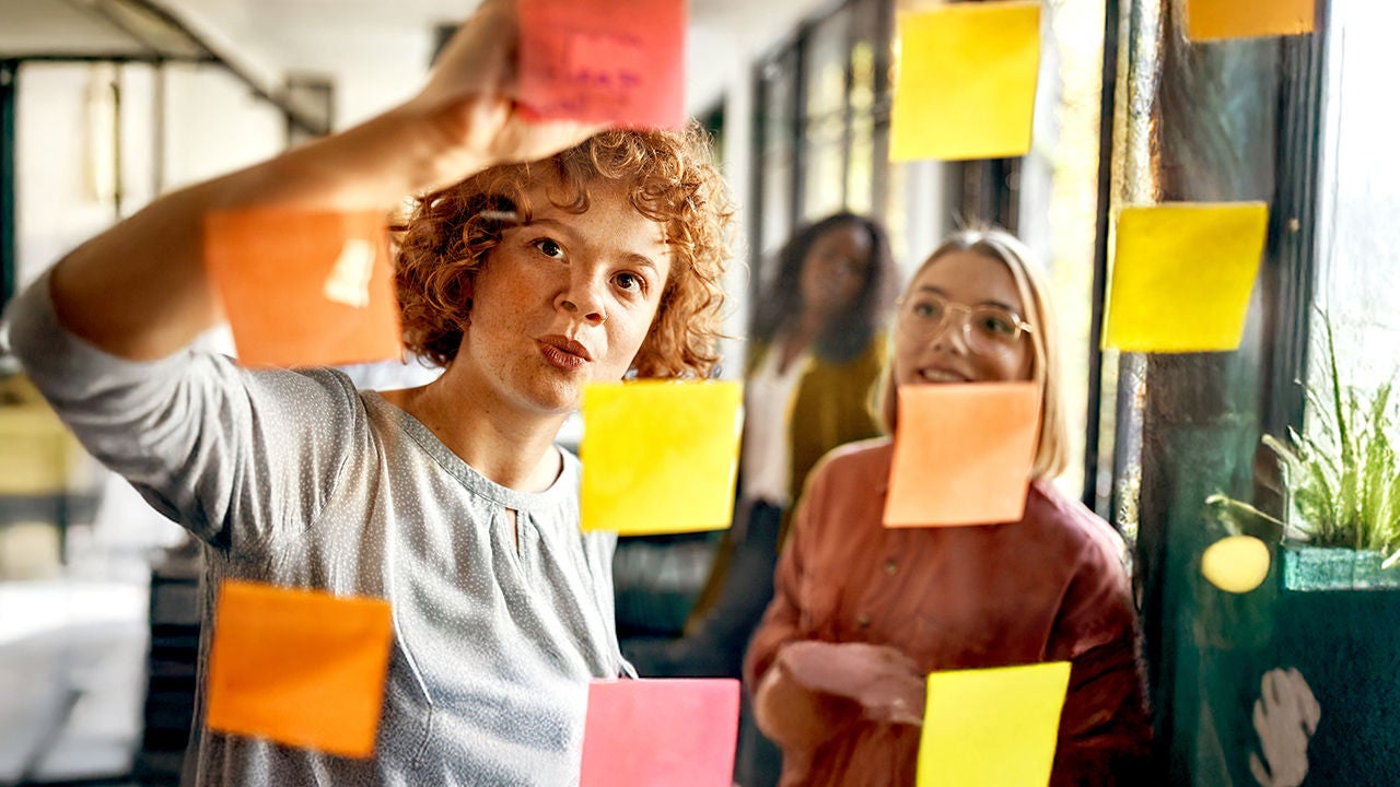 Three women brainstorming in front of a vision board