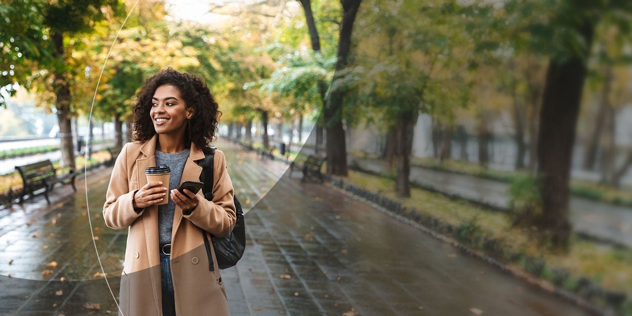 امرأة تحمل قهوة وهاتفًا ذكيًا أثناء المشي في الحديقة.