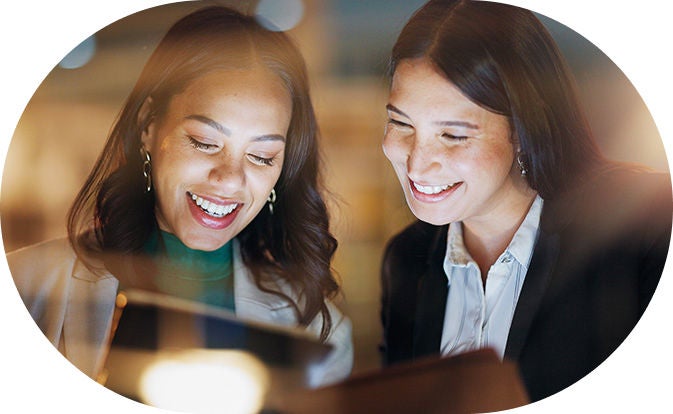 Two women smiling and looking at a screen, showcasing collaboration in a positive work environment.