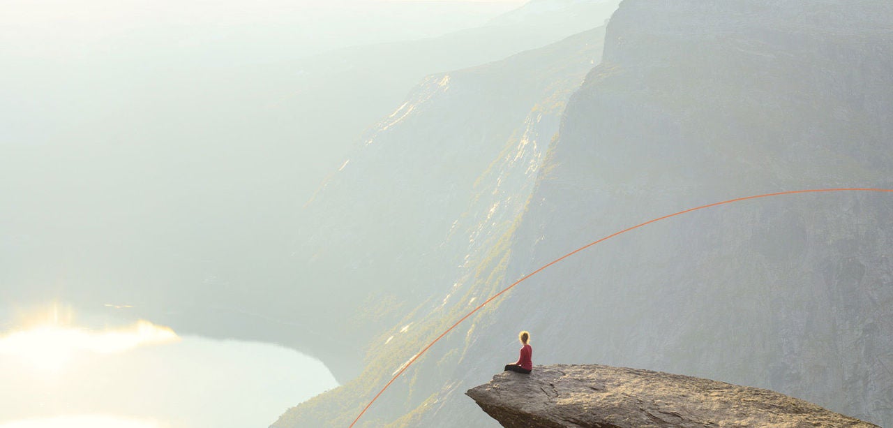 En person sidder alene på en klippe og ser ud over et vidstrakt bjerglandskab.