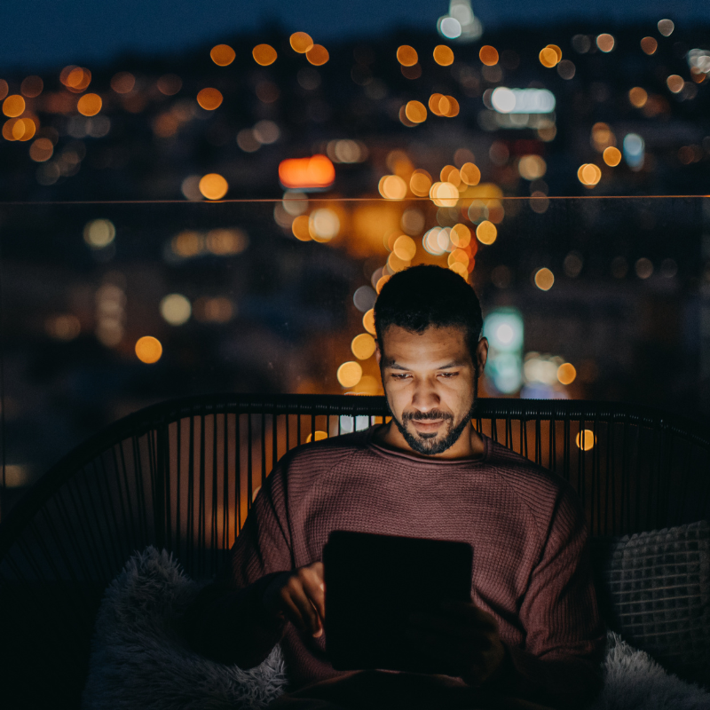 A man looks at his tablet on a balcony at night. 