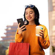 happy young asian woman with phone and coffee in her hands.