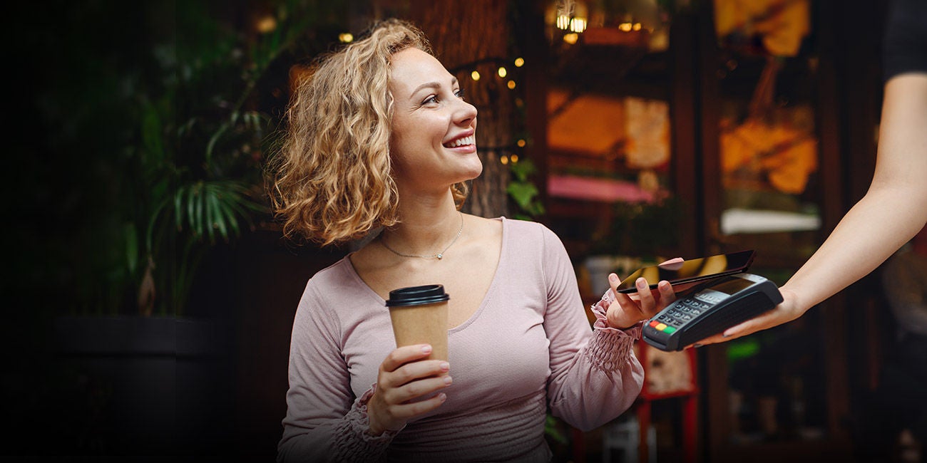 Ženska osoba u kafiću drži kafu i plaća mobilnim uređajem.