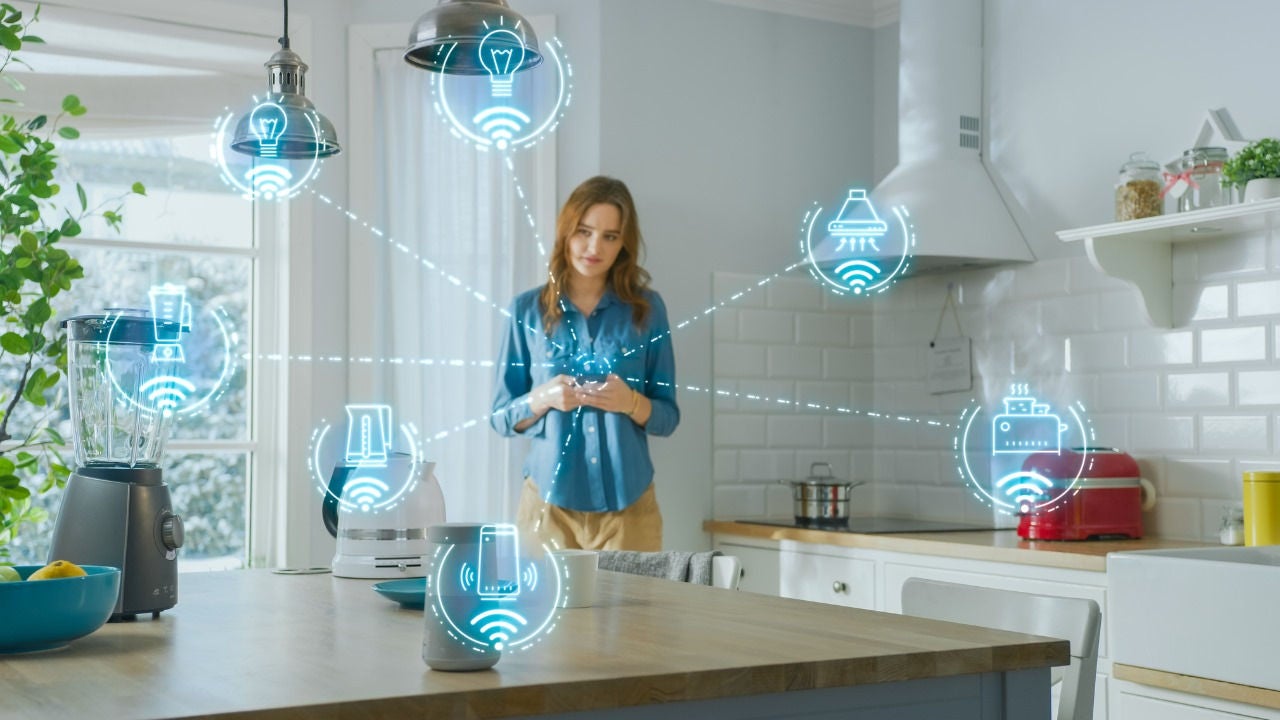 A woman looks at her phone in her kitchen with a graphic overlay showing which appliances are Wi-Fi connected. 