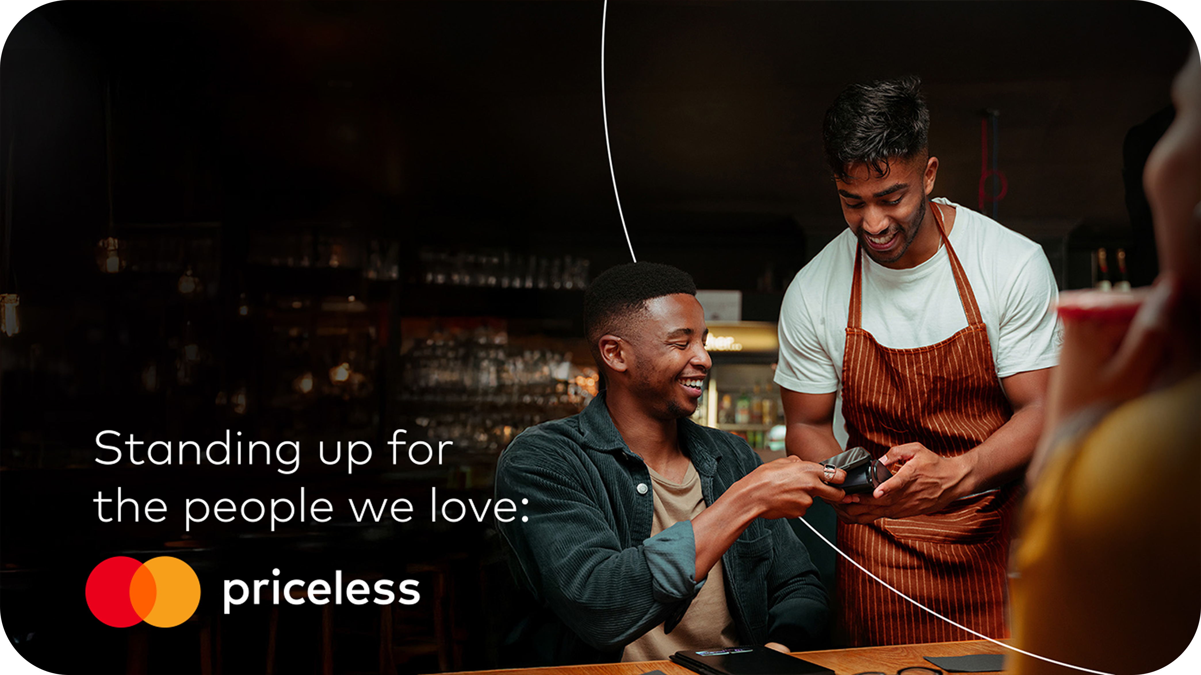 A smiling man taps his Mastercard to pay at a cafe, showing how easy it is to stand up for the people we love with Priceless.