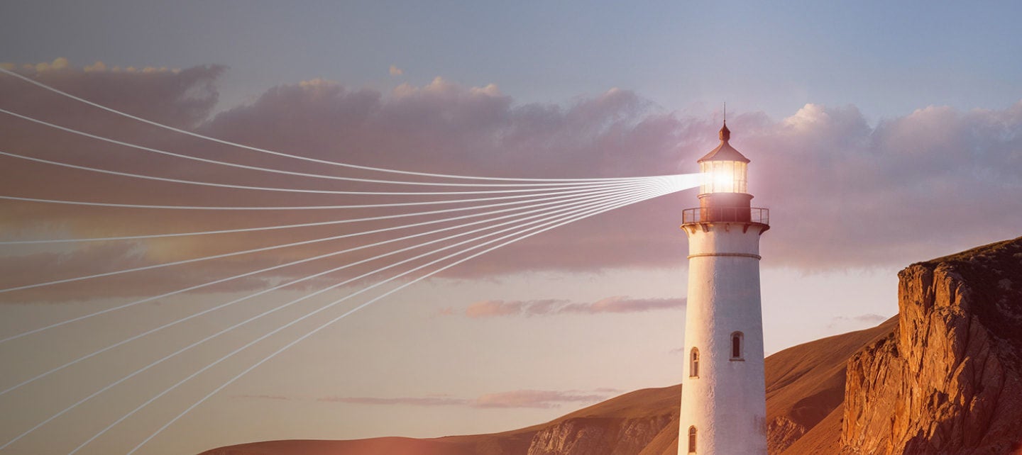 lighthouse shining light beams at sunset
