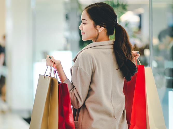 A smiling young woman looks over her shoulder while carrying multiple shopping bags, demonstrating the link between consumer sentiment and spending.