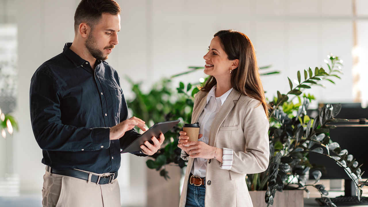 A man on a tablet talking to a woman holding coffee