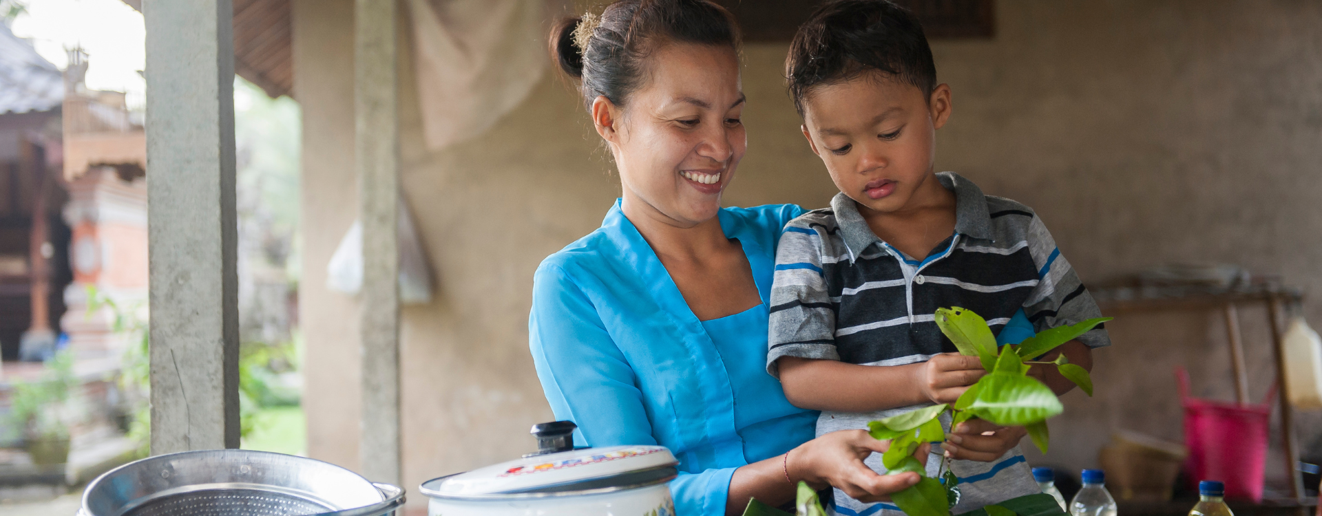 A woman holds a young boy in an outdoor kitchen. 
