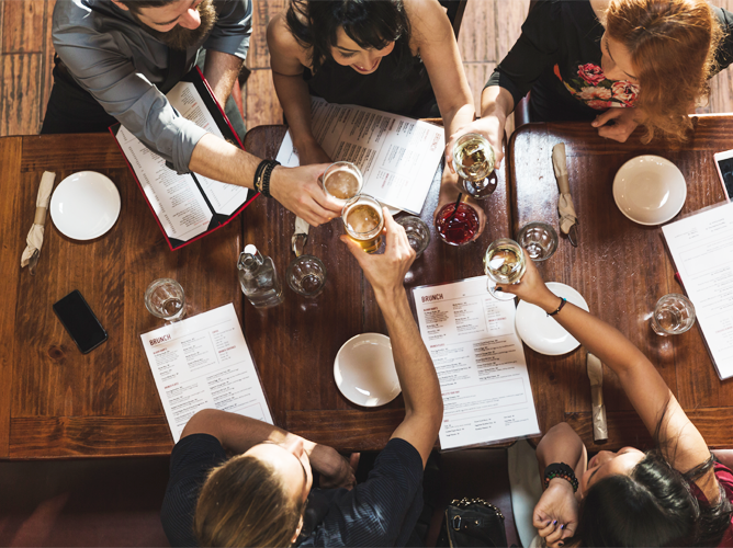 An overhead view of friends toasting with drinks at a restaurant, representing consumer holiday spending on social experiences.
