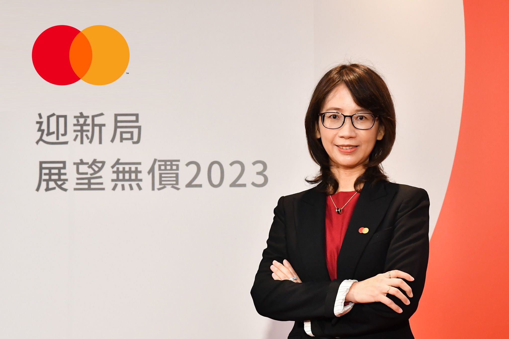 A woman in a black blazer stands with her arms crossed, smiling in front of a white and red backdrop with Chinese text and a brand logo.
