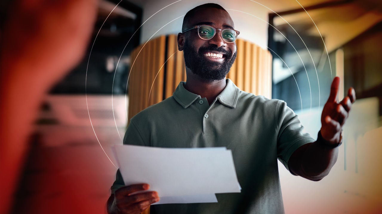 Smiling Black man in glasses holding papers, gesturing confidently.