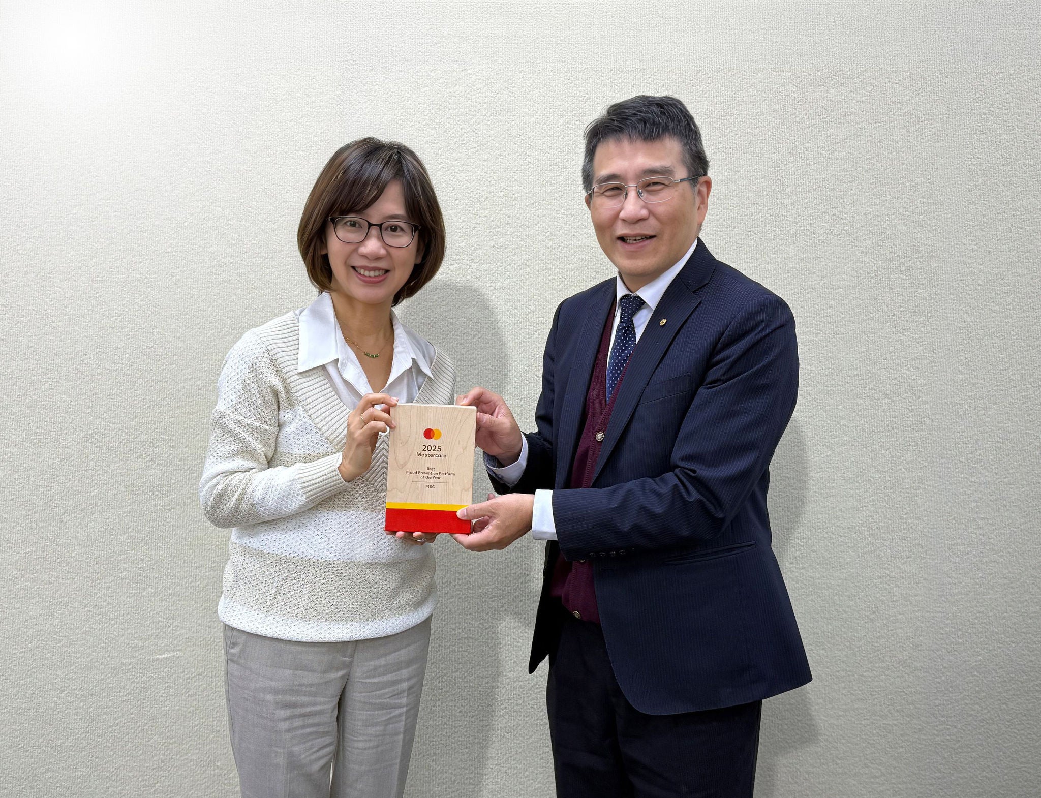 A woman and a man in business attire stand side by side holding a wooden award plaque together, smiling at the camera.