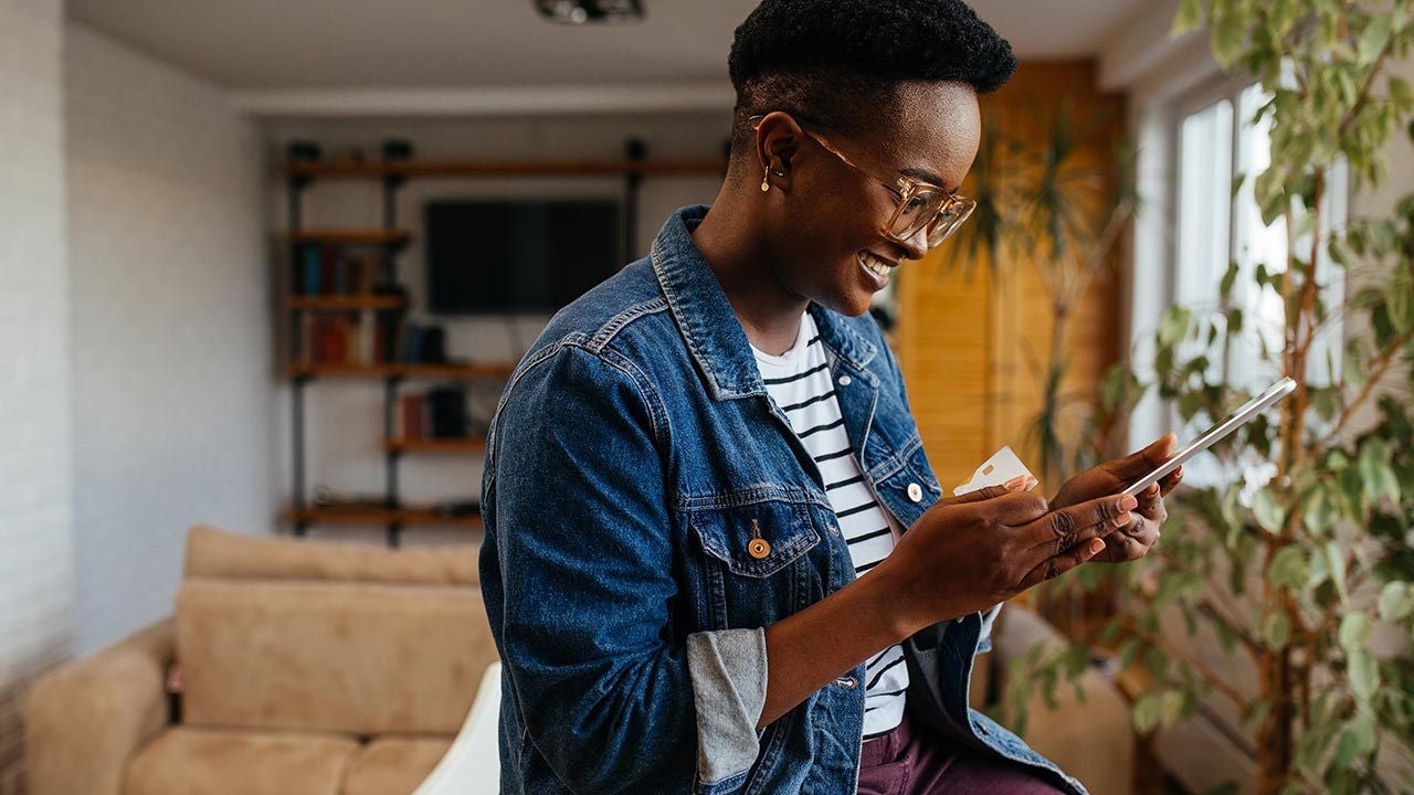A woman smiles at her phone in her home. 