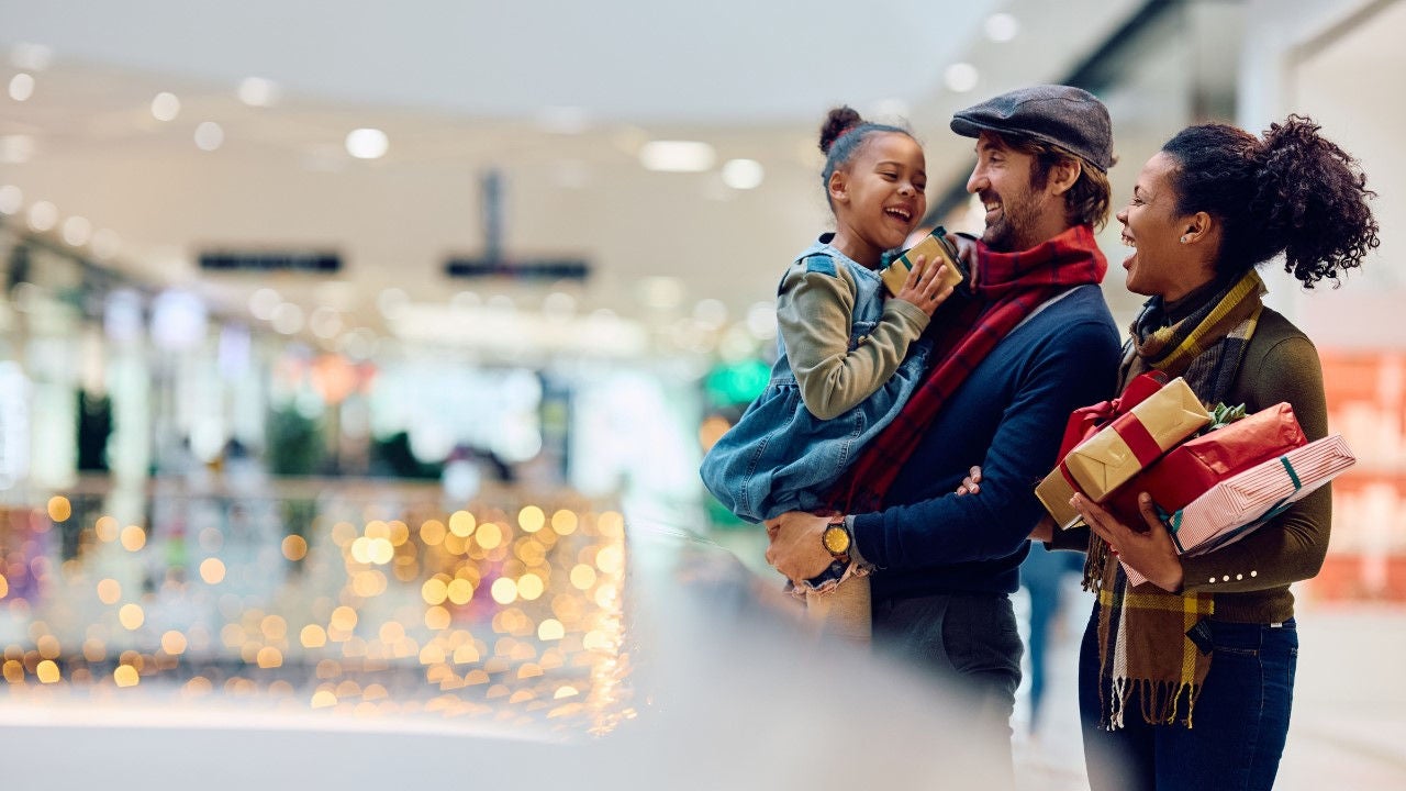 A family holding gifts laughs in a mall decorated for the holiday season. 