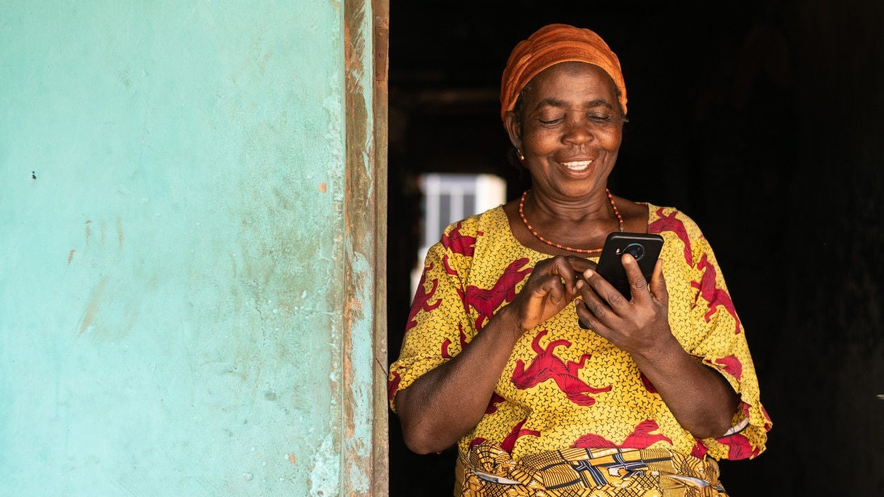 A woman in African print dress standing in a doorway looking at her phone. 