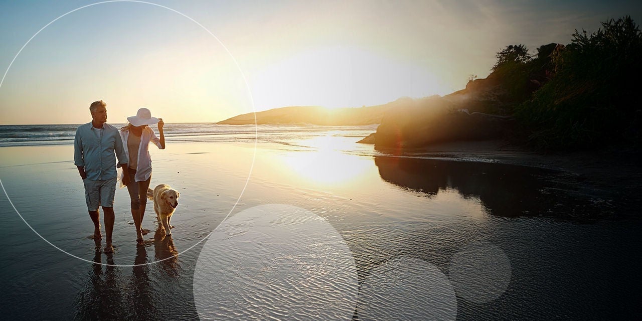 זוג מבוגרים מטייל עם כלב בחוף הים.