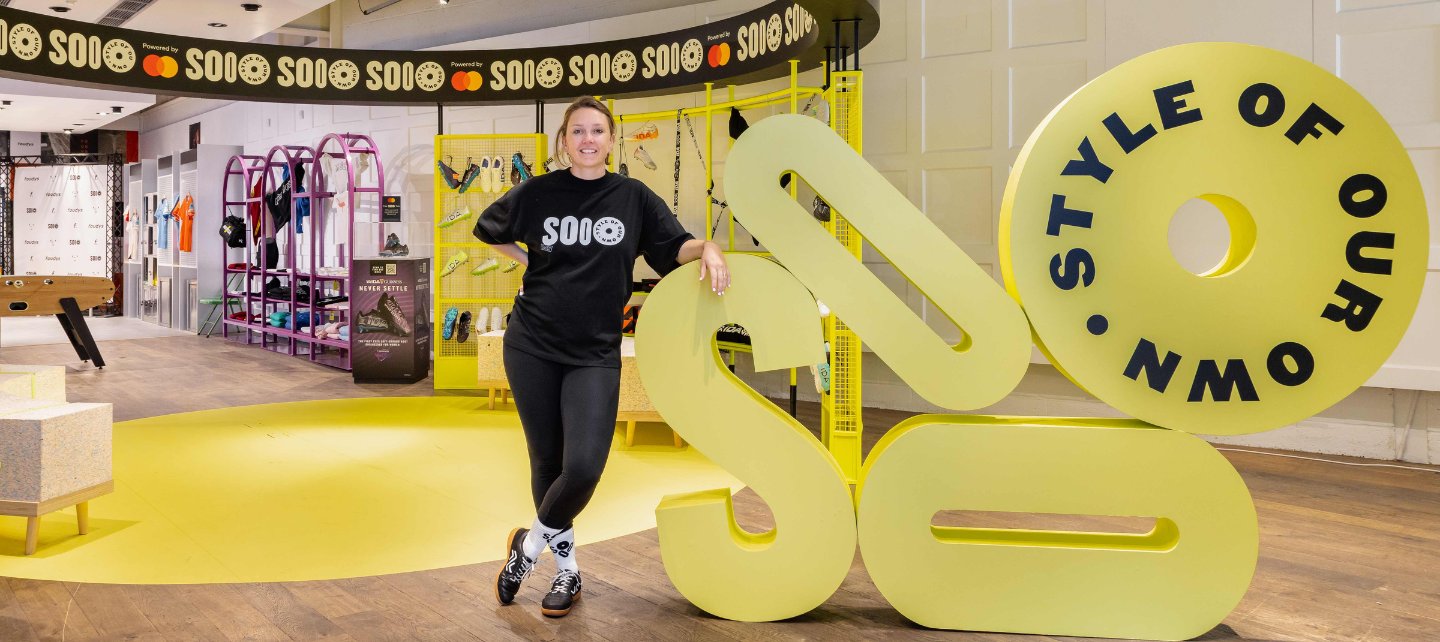 Laura Youngson bär en SOOO T-shirt inuti SOOO popup-butiken med klädställ och montrar i bakgrunden. 