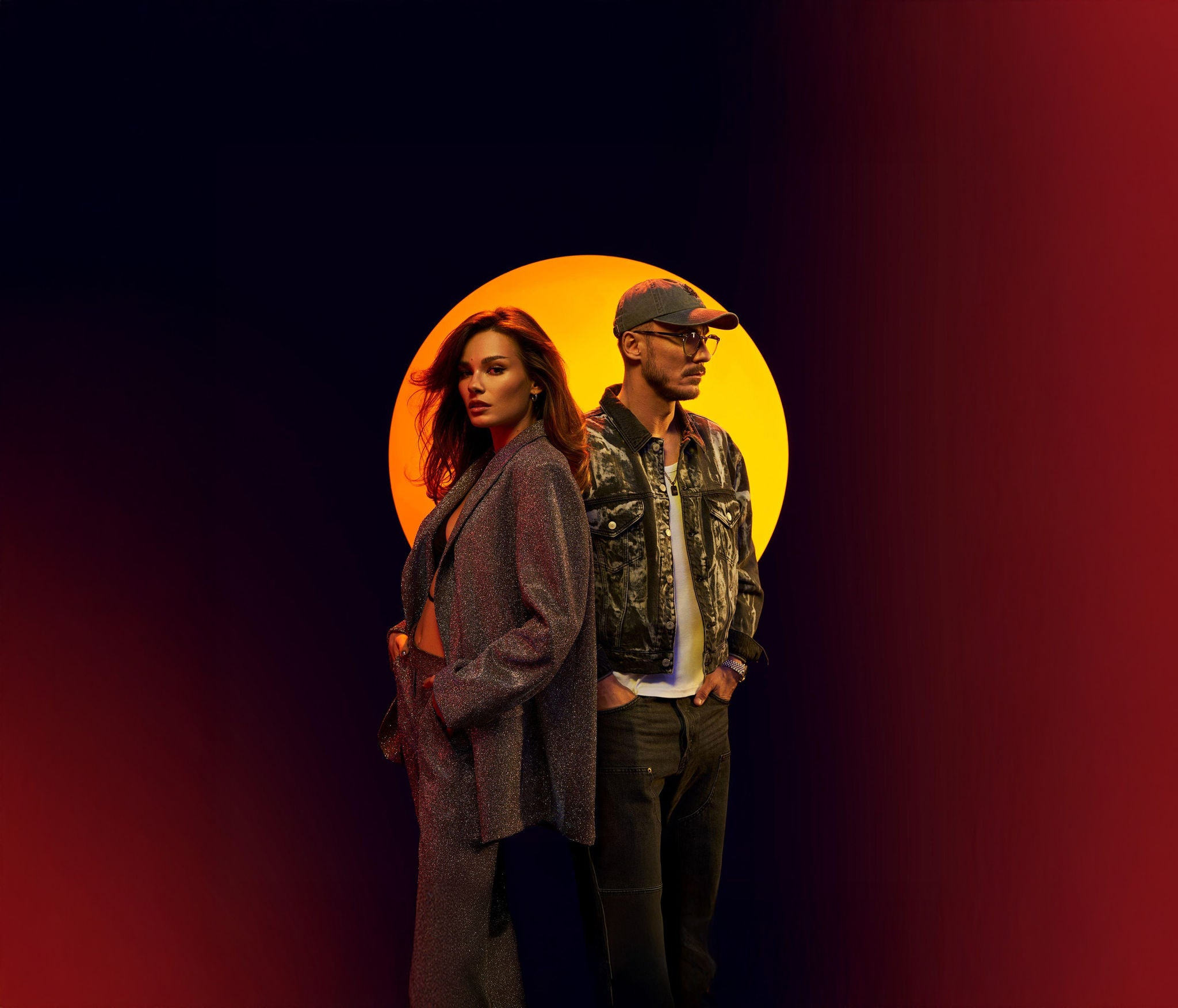 Dwie osoby w modnych stylizacjach na tle żółto-czerwonego okręgu.