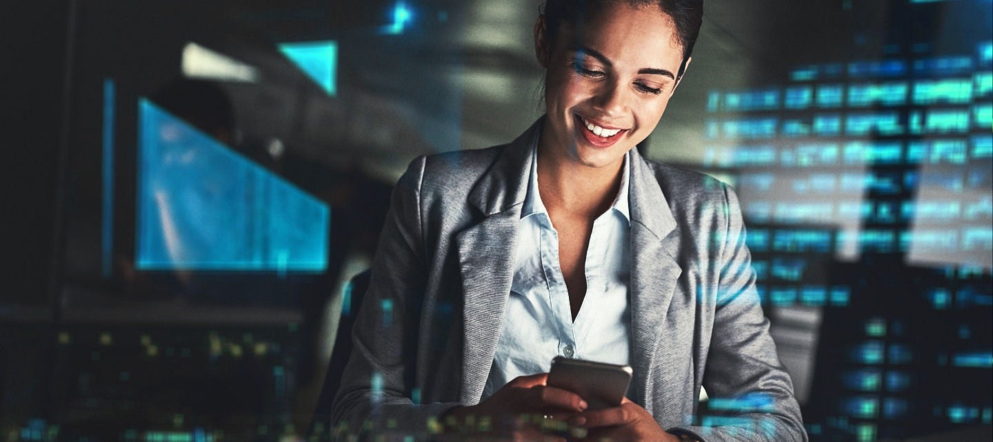 A woman locks at her phone at night in an office. 