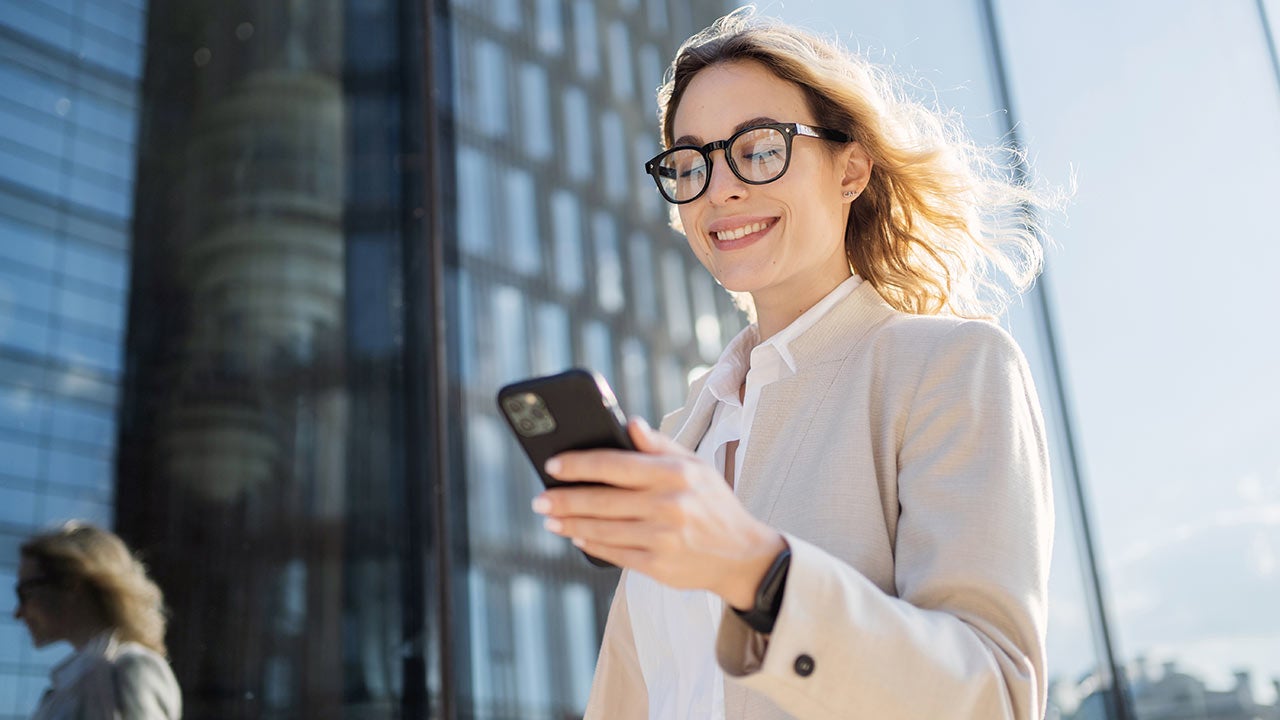 Business woman walking with phone in city.
