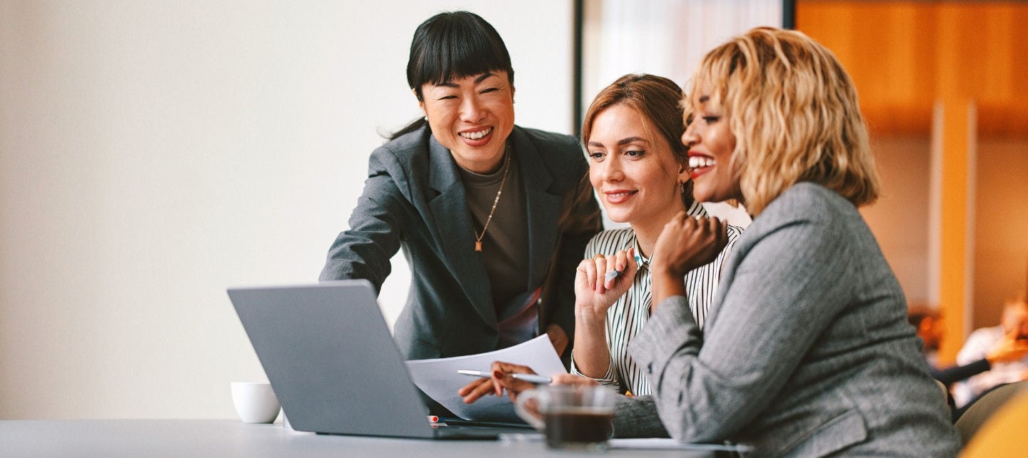 Three businesswoman sit around a laptop. 
