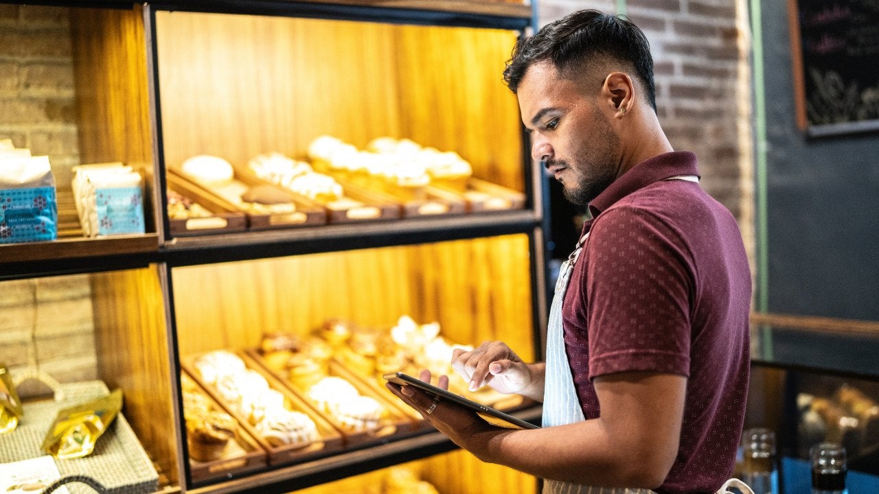 A man looks at a tablet in front of a display of baked goods. 