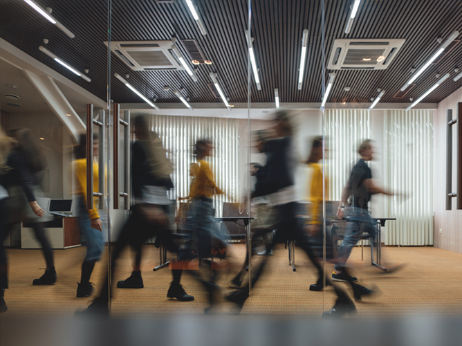 A motion-blur image of people walking through a modern office space, illustrating how a busy job market grows when consumers spend.
