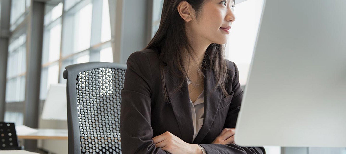 En person i dressjakke som ser ut av vinduet mens de sitter ved et skrivebord med en datamaskin.