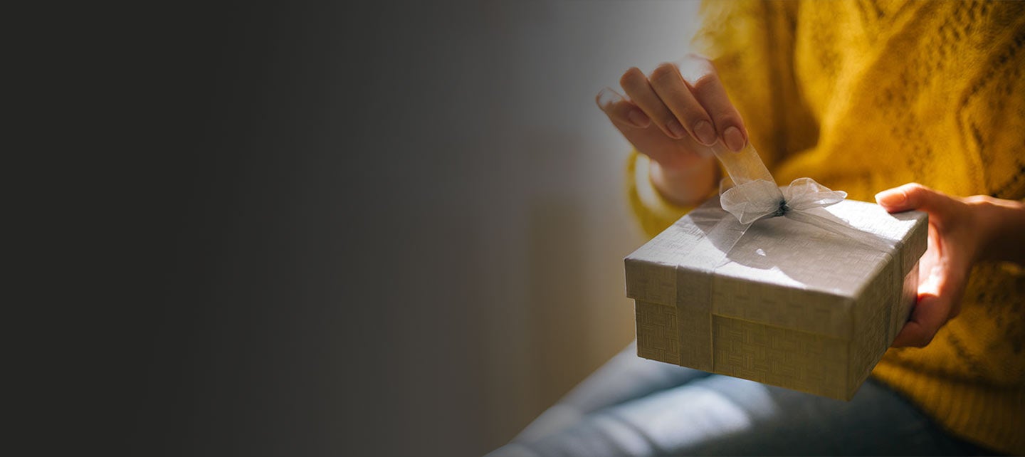 Person unwrapping a bow on a wrapped gift box containing a Mastercard gift card.