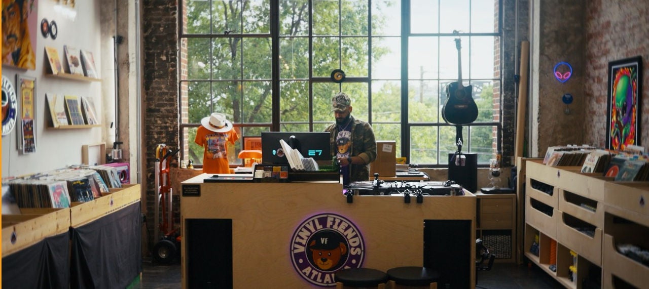 DJ Silver Knights looks at his computer among his record collection in front of a large window. 