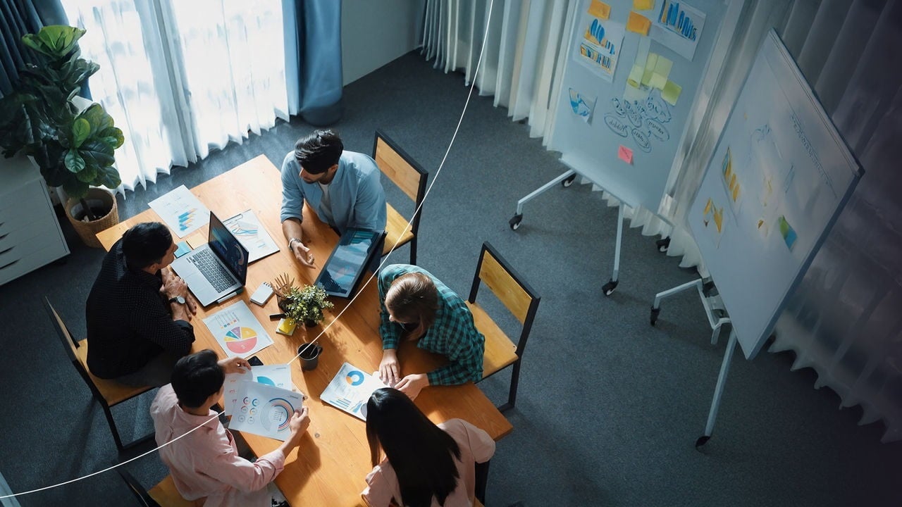 תצוגה עליונה של עמיתים לעבודה בחדר ישיבות שדנים במסמכים ובתרשימים ליד שולחן.