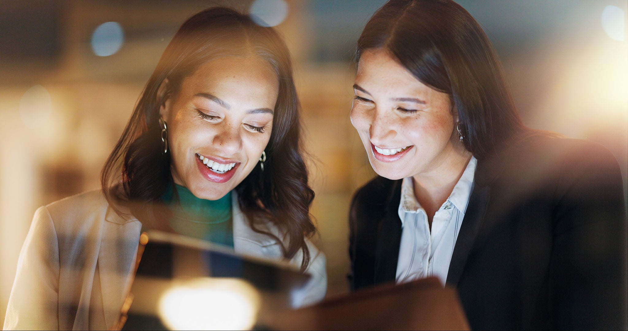 Laptop, tablet and collaboration with business people at night in the office together for teamwork. Technology, smile and a happy employee team of women working on a project or report in the evening.