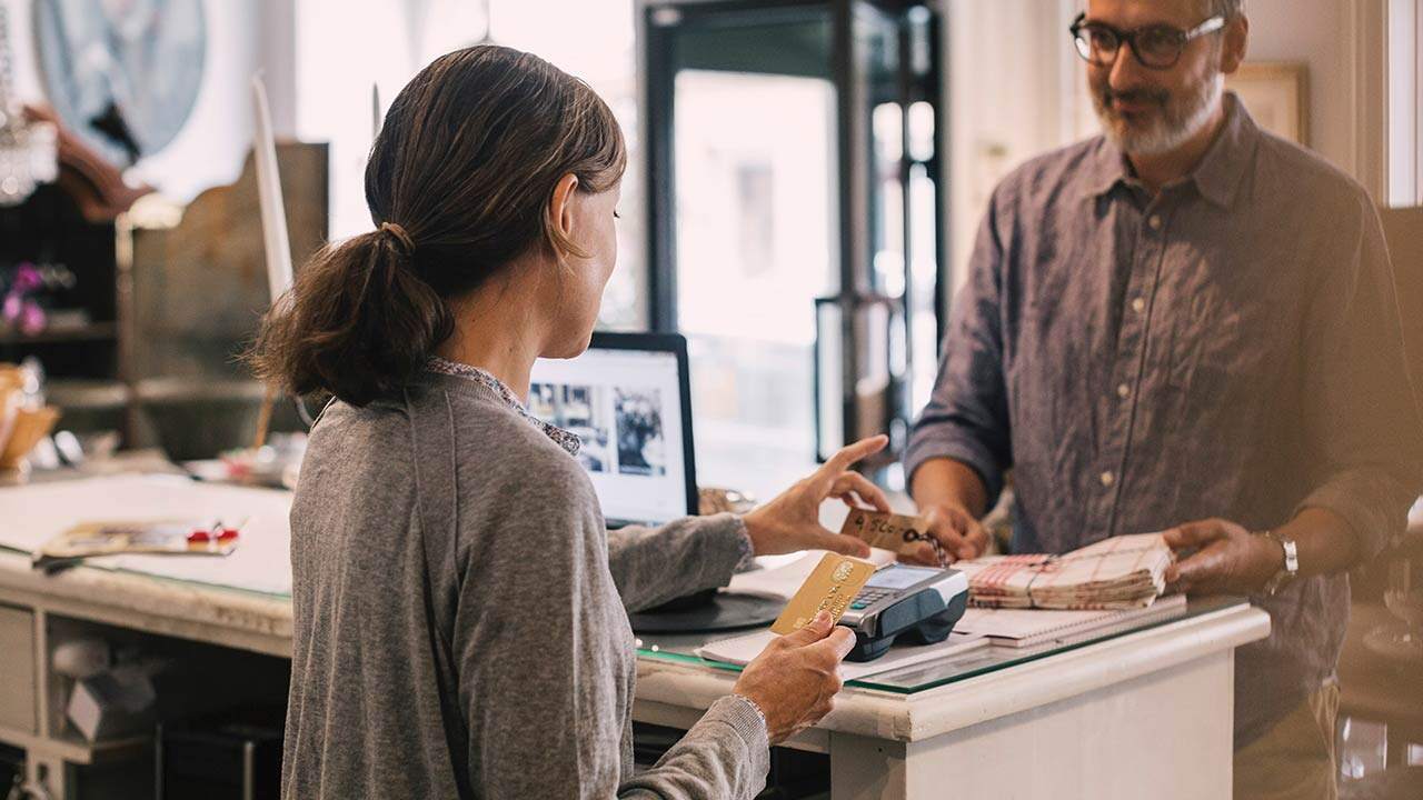 Vásárló bankkártyával fizet egy üzlet pénztáránál, miközben az eladó átveszi a fizetést a terminálnál