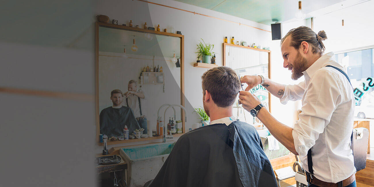 Fodrász egy férfi haját vágja egy modern barber shopban, háttérben tükörrel és fodrászeszközökkel.
