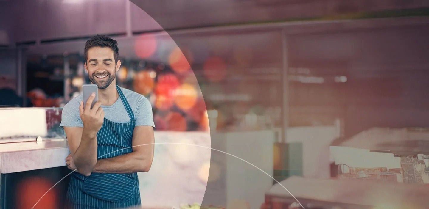 גבר בסינר מביט בטלפון הסלולרי.