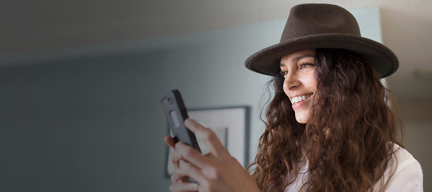 Woman with hat holding her phone and smiling