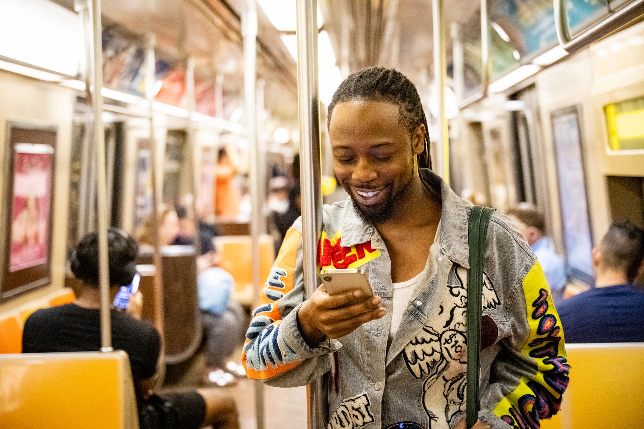 Smiling man with dreadlocks standing on a moving subway train while looking down at his smartphone.