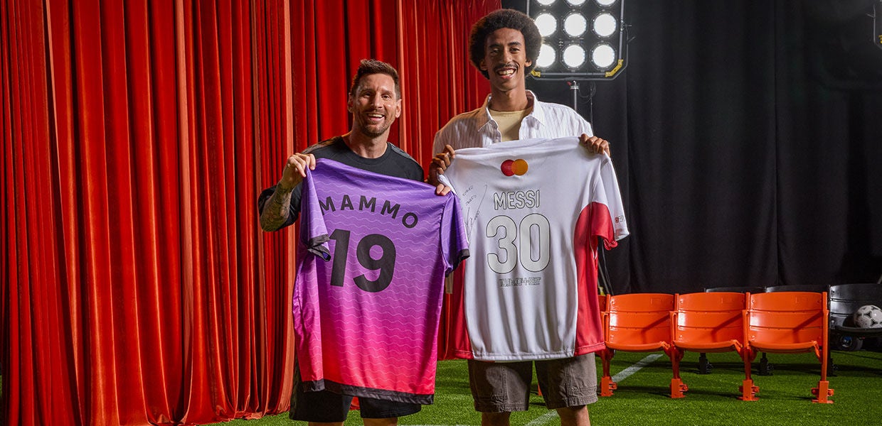 Lionel Messi and a happy fan posing together on a stage set. Messi holds a purple and pink "Mammo 19" jersey, while the fan holds a white and red signed "Messi 30" jersey featuring the MasterCard logo.