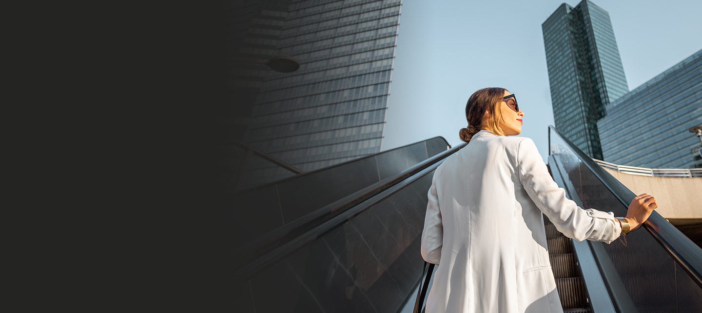 Businesswoman riding an outdoor escalator among skyscrapers.