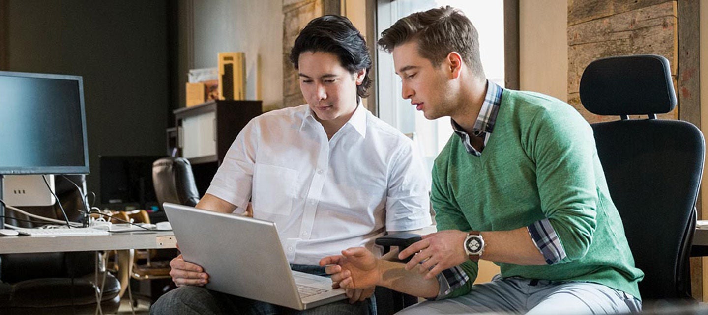 To personer som ser på en bærbar datamaskin i et kontormiljø.