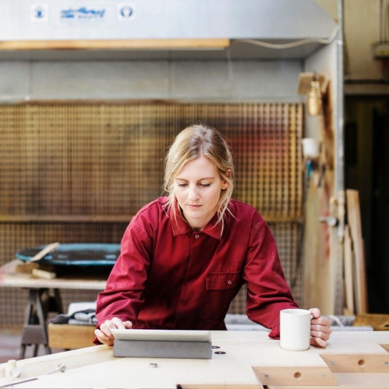A small business owner looks at a digital pad while holding a cup of coffee. 